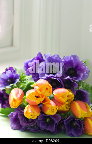 Ein Bündel von orange und lila Tulpen am grünen Tisch von einem Fensterbrett. Stockfoto