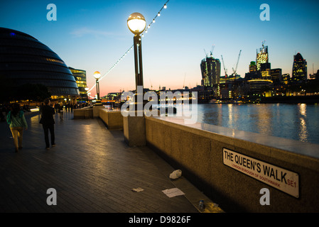 Queens Walk City Hall beleuchtete Skyline Abenddämmerung London Vereinigtes Königreich / LONDON, Vereinigtes Königreich - Fußgänger navigieren auf dem Queen's Walk in der Abenddämmerung, vorbei an der Glasfassade des London City Hall am Südufer der Themse. Die von Norman Foster entworfene, modifizierte kugelförmige Form des Gebäudes minimiert die Oberfläche, um den Wärmeverlust zu reduzieren. Auf der anderen Seite des Wassers erhebt sich die 20 Fenchurch Street im Bau und nutzt ein schweres Design, um die Bodenfläche in den lukrativeren oberen Stockwerken zu maximieren. Stockfoto