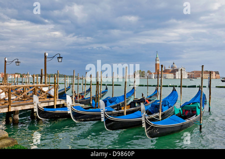 Gondeln warten auf Touristen in der Nähe von Piazza San Marco in Venedig. Zeigen Sie mit dramatischer Himmel in Richtung San Giorgio Maggiore an. Stockfoto