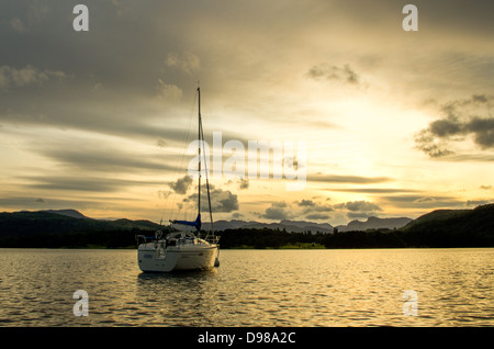 Ein einsames Boot auf Windermere während des Sonnenuntergangs mit Langdale Pikes in der Ferne. Stockfoto