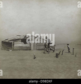 Sturm in der Dust Bowl, Amerika, um 1930. Und jungen Mann zu Fuß in Richtung Holzhütte schrittweise durch Wind geblasen Staub bedeckt. Kleiner Junge hält seine Hand sein Gesicht zu schützen. Stockfoto