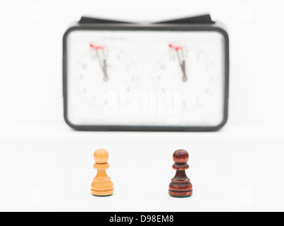 Studioaufnahme von Schachfiguren, weiße und schwarze Figur mit Schachuhr im Hintergrund. Stockfoto