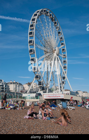 Menschen entspannend am Kiesstrand, mit den Brighton Rad im Hintergrund, an einem warmen, sonnigen Tag im Frühherbst. Südküste von England, UK. Stockfoto