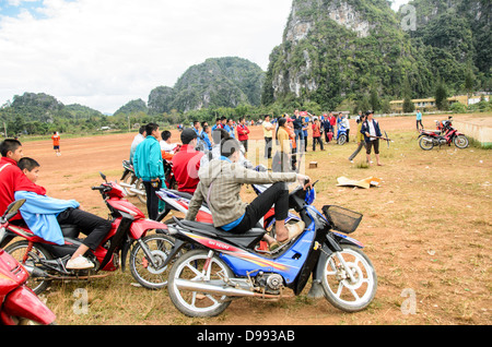 VIENG XAI, Laos — die Zuschauer der Studenten stellen sich auf ihren Scootern und Fahrrädern an, um auf einem unbefestigten Spielfeld in der Nähe von Vieng XAI im Nordosten von Laos einen Armbrustwettbewerb anzuschauen. Die lokale Veranstaltung zieht Teilnehmer und Zuschauer aus den umliegenden Dörfern dieser ländlichen Region an. Stockfoto