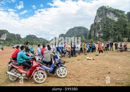 Crossbow Contest Zuschauer Vieng XAI Laos // VIENG XAI, Laos — Studenten stellen sich auf ihren Scootern und Motorrädern an, um einen Crossbow-Wettbewerb zu sehen, der auf einem unbefestigten Spielfeld im rauen Gelände in der Nähe von Vieng XAI im Nordosten von Laos stattfindet. Die traditionelle Sportveranstaltung zieht Teilnehmer und Zuschauer aus den umliegenden Dörfern dieser ländlichen Bergregion an. Vieng XAI, in der Provinz Houaphanh gelegen, ist bekannt für seine Kalksteinkarstlandschaft und das Höhlennetz, das während des Zweiten Indochina-Krieges als Hauptquartier für die Pathet Lao diente. Die Stadt liegt nahe der Grenze zu Vietnam Stockfoto