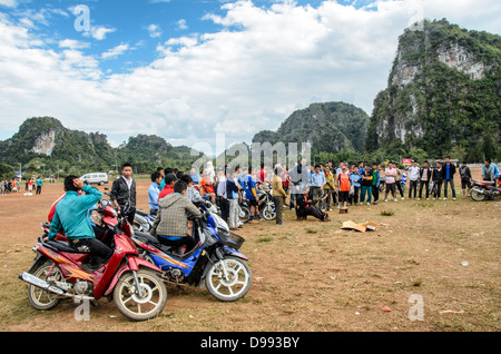 Crossbow Contest Zuschauer Vieng XAI Laos // VIENG XAI, Laos — Studenten stellen sich auf ihren Scootern und Motorrädern an, um einen Crossbow-Wettbewerb zu sehen, der auf einem unbefestigten Spielfeld im rauen Gelände in der Nähe von Vieng XAI im Nordosten von Laos stattfindet. Die traditionelle Sportveranstaltung zieht Teilnehmer und Zuschauer aus den umliegenden Dörfern dieser ländlichen Bergregion an. Vieng XAI, in der Provinz Houaphanh gelegen, ist bekannt für seine Kalksteinkarstlandschaft und das Höhlennetz, das während des Zweiten Indochina-Krieges als Hauptquartier für die Pathet Lao diente. Die Stadt liegt nahe der Grenze zu Vietnam Stockfoto