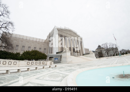 Renovierung des Supreme Court-Gebäudes Washington DC | WASHINGTON D.C., Vereinigte Staaten — Gerüste und bedrucktes Segeltuch verdecken den Flügel und den Portikus des Gebäudes des Obersten Gerichtshofs der Vereinigten Staaten, gesehen von seinem westlichen Platz neben einem flachen Spiegelbecken. Das 1935 errichtete Gerichtsgebäude, entworfen von Cass Gilbert, liegt in der Nähe der Library of Congress, die rechts hinter den Bäumen sichtbar ist. Stockfoto