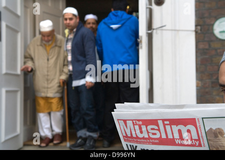 Einwanderer UK 2010s Männer, die Freitagsgebete verlassen, Jamme Masjid Moschee, Brick Lane, London E1. Ein Mann liest eine kostenlose Kopie von The Muslim, The Voice of Muslims 2013 UK 2010s HOMER SYKES Stockfoto