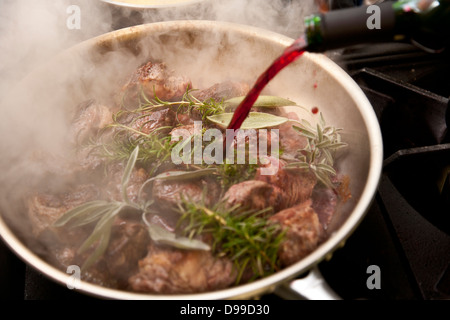 Geschmortes Fleisch in einer Pfanne mit frischen Kräutern und Rotwein Stockfoto