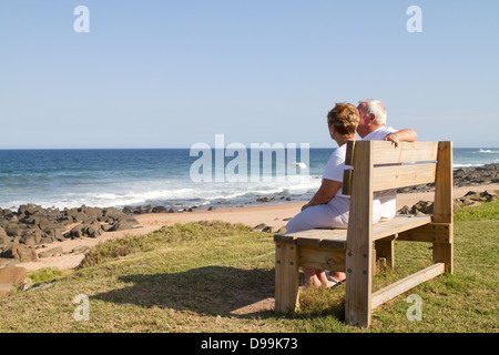 Älteres Paar auf Strand-Bank sitzen Stockfoto