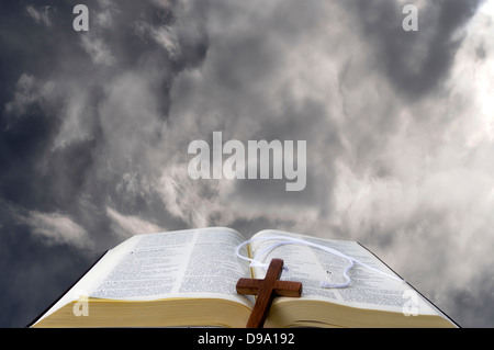 Öffnen Sie Bibel gegen die Wolken mit einem hölzernen Kreuz Stockfoto