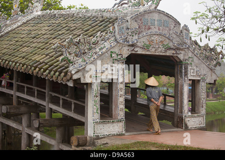 Frau in konische Hut überqueren Thanh Toan Fußgängerbrücke in Thuy Thanh Dorf außerhalb von Hue, Provinz Thừa Thiên-Huế, Vietnam Stockfoto