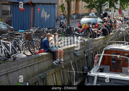 Junge Leute und Studenten genießen Sie Erfrischungen in gemütlicher Atmosphäre in der Sonne an Christianshavn Kanal, Kopenhagen, Dänemark, an einem warmen Samstag Nachmittag. Stockfoto