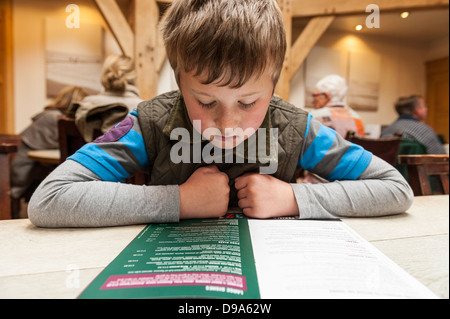 Ein 9-jähriger Junge schaut das Menü im Byfords Café in Holt, Norfolk, England, Großbritannien, Uk Stockfoto