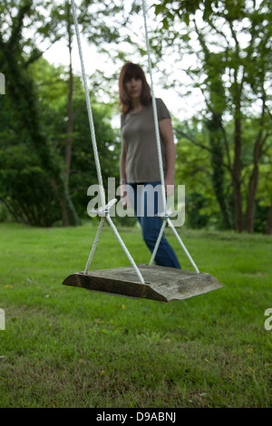 Eine nachdenkliche Frau, Blick auf eine leere Gartenschaukel. Stockfoto