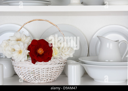 Nahaufnahme eines Korbs von Rosen auf dem Regal einen Schrank voller weißen Platten. Elemente enthalten, Teller, Untertassen, Schalen Stockfoto