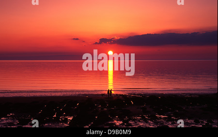 Hunstanton Beach - Paar in Silhouette vor einem wunderschönen Sonnenuntergang, wenn die Sonne im Meer widerspiegelt, Norfolk, England, UK. Stockfoto