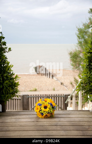 Brautstrauss mit Sonnenblumen auf Holzstufen Strandhaus für Hochzeiten mit Blick auf Strand und Meer im Hintergrund Stockfoto