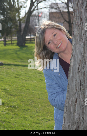Eine sehr attraktive Frau spähen aus hinter einem Baum Stockfoto