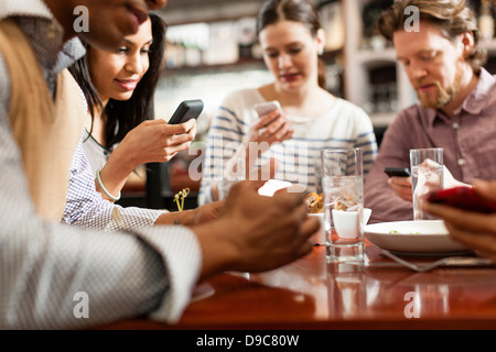 Freunden im Restaurant SMS und Anzeige von Fotos über Handys Stockfoto
