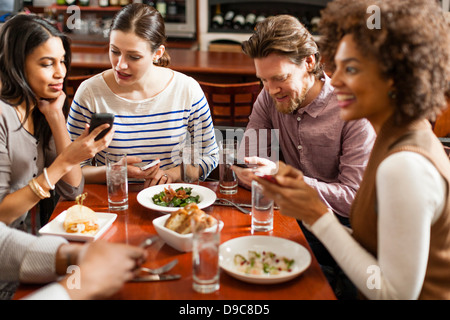 Freunden im Restaurant SMS und Anzeige von Fotos über Handys Stockfoto