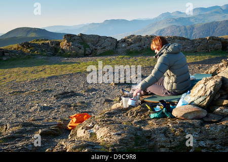 Ein Wanderer, Kochen auf einem Campingkocher auf dem Gipfel des Robinson im Lake District. Stockfoto