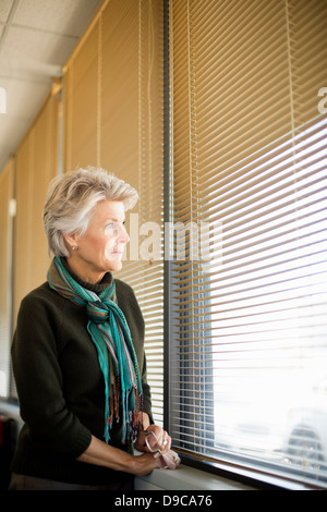 Ältere Frau, die durch Fenster Stockfoto