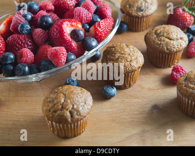 Obst-Muffins gebacken frisch auf einem Holztisch neben frischen Erdbeeren, Himbeeren und Heidelbeeren. Stockfoto