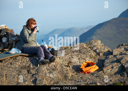 Eine weibliche Wanderer genießen eine frühen Morgen Tasse Tee nach camping auf dem Gipfel des Robinson im Lake District Stockfoto