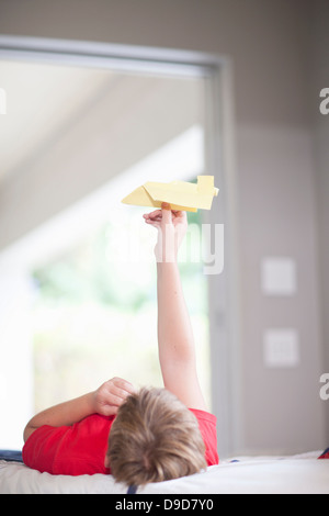 Junge im Bett spielen mit Papier Flugzeug Stockfoto