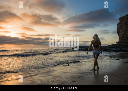 Junge Frau, die zu Fuß am Strand bei Sonnenuntergang, Rückansicht Stockfoto