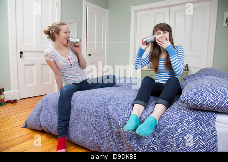 Mädchen sitzen auf Bett mit Tincan Telefon spielen Stockfoto