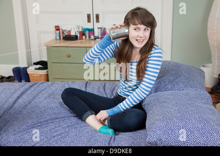 Mädchen sitzen auf Bett mit Blechdose Telefon spielen Stockfoto