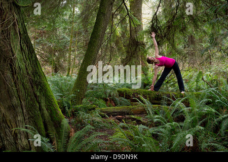 Reife Frau, die Durchführung von Dreieck-Pose im Wald Stockfoto