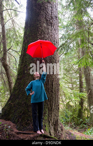 Reife Frau mit roten Regenschirm im Wald Stockfoto