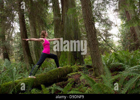 Reife Frau, die Durchführung von Krieger-Pose im Wald Stockfoto