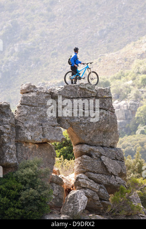 Junger Mann stehend auf Felsformation mit Mountainbike Stockfoto