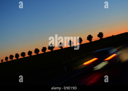 Ein Auto fährt auf einer Landstraße bei Sonnenuntergang in der Nähe von Bad Blankenburg, Deutschland, 5. Juni 2013 mit Bäumen gesäumt. Foto: Marc Tirl Stockfoto