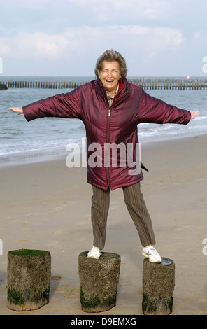 Senior mit der Strandspaziergang im Herbst. Steht in der Weise mit ausgestreckt Arme auf Wellenbrecher und Klammern sich in den Wind. (M Stockfoto