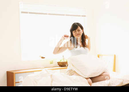 Frau sitzt auf Bett Strecken Arme Stockfoto
