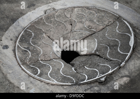 Alten gebrochenen Kanaldeckel auf der schmutzigen Asphaltstraße Stockfoto