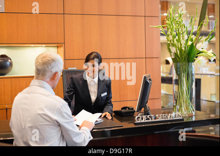 Unternehmer im Gespräch mit Empfangsdame an der Hotel Rezeption Theke Stockfoto