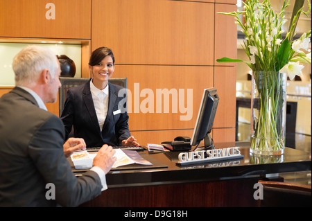 Unternehmer im Gespräch mit Empfangsdame an der Hotel Rezeption Theke Stockfoto