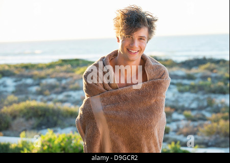 Glücklicher Mann eingewickelt in einem Tuch steht am Strand Stockfoto