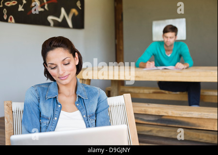 Frau mit einem Laptop mit ihrem Mann im Hintergrund Stockfoto