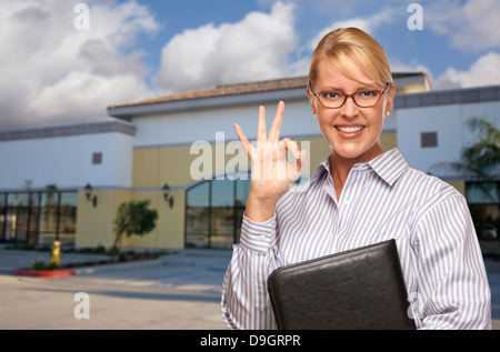 Lächelnde Geschäftsfrau geben Okay Zeichen vor der vakanten Bürogebäude. Stockfoto