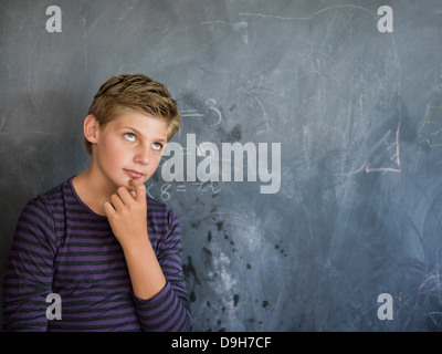 Jungen denken vor einer Tafel im Klassenzimmer Stockfoto