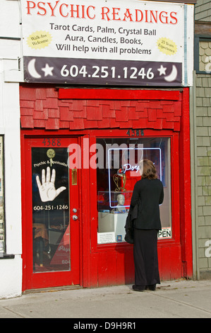 Frau in Schwarz gekleidet, die in das Fenster eines psychischen Messwerte und okkulte Shop auf der Main Street in Vancouver, BC, Kanada Stockfoto
