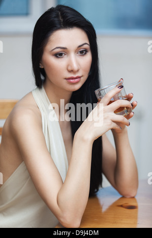 Das Mädchen sitzt an einem Tisch mit einem Glas Whiskey Stockfoto