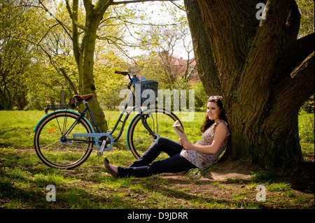 Junge kaukasische Frau sitzt unter einem Baum und entspannt ein Buch zu lesen. Stockfoto